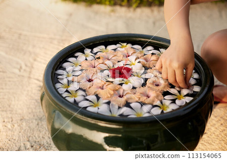 Woman makes decor arrangement in green bowl on the water of frangipani plumeria flowers. Isolated view of hands and floristic composition. Aroma spa concept. 113154065