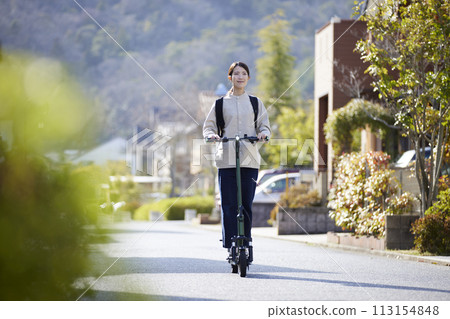 A Japanese woman riding an electric scooter through a residential area 113154848