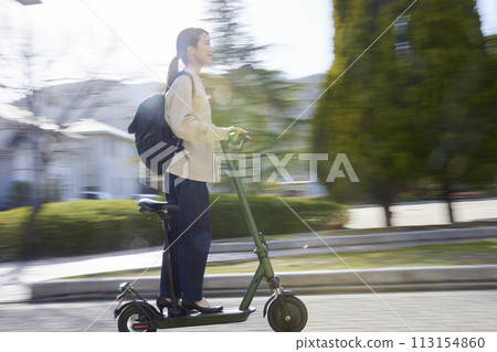A Japanese woman riding an electric scooter through a residential area 113154860