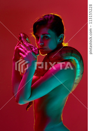 Fantasy and dreams. Beautiful young shirtless woman with slim body posing with snake against red studio background in neon light Fantasy and dreams. Beautiful young shirtless woman with slim body posing with snake against red studio background in neon light 113155228