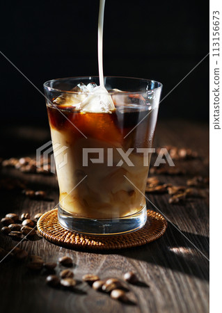 cold milk poured into iced coffee 113156673
