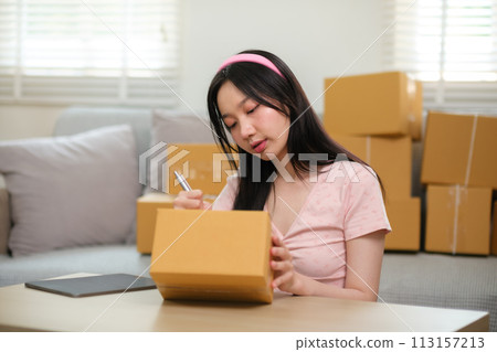 Startup small business owner working at home, woman writing address on parcel box at home for delivery order to customer, Online shopping business, ecommerce concept 113157213
