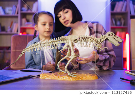 Two female sitting together at table and make model of tyrannosaurus. 113157456