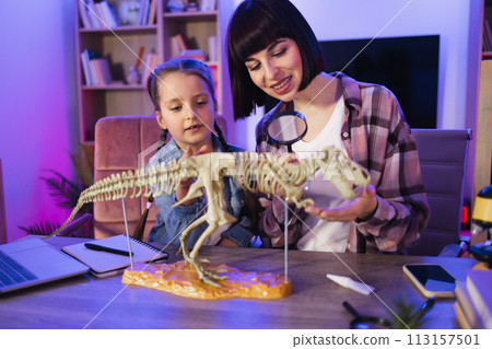 Focused young woman examine skeleton of dinosaur with magnifying glass. Focused young woman examine skeleton of dinosaur with magnifying glass. 113157501