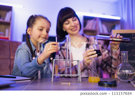 Caring woman and small kid girl improving knowledge at evening home. 113157684