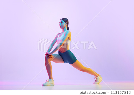 Young athlete woman doing lunges in motion in neon light against gradient studio background. Side view portrait. Young athlete woman doing lunges in motion in neon light against gradient studio background. Side view portrait. 113157813