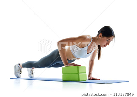 Young, fit, strong woman in legging and top doing push-ups with blocks for yoga against white studio background. 113157849