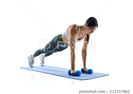 Young, fit, strong woman in legging and top doing push-ups with dumbbell pulls against white studio background Young, fit, strong woman in legging and top doing push-ups with dumbbell pulls against white studio background 113157862