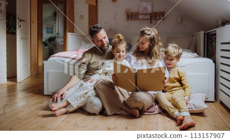 Beautiful family sitting in kids room on floor, looking at old family photos in photoalbum. Calm hygge family moment. 113157907