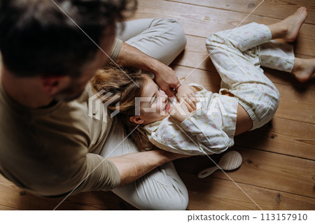 Top view of father with daughter on floor laughing together, having fun, tickling each other. Girls dad. Unconditional paternal love, Father's Day concept. 113157910