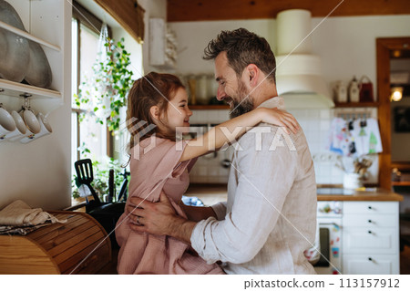 Daughter hugging father lovingly, sitting on kitchen counter. Unconditional paternal love, Father's Day concept. 113157912