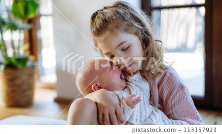 Portrait of big sister soothing newborn sister. Girl taking care of crying baby. Sisterly love, joy for new family member. 113157923