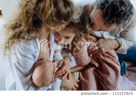 Mother breastfeeding newborn, big sister looking at new baby in mom's arms. Strong family, bonding and parents' unconditional love for their children. Mother breastfeeding newborn, big sister looking at new baby in mom's arms. Strong family, bonding and parents' unconditional love for their children. 113157924