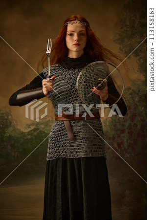 Young red haired girl-knight posing holding serving fork and lid like sword and shield against vintage studio background. Young red haired girl-knight posing holding serving fork and lid like sword and shield against vintage studio background. 113158163