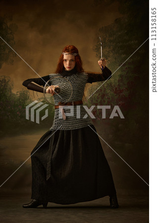 Redhaired princess knight posing holding serving fork and lid like sword and shield against vintage studio background. Redhaired princess knight posing holding serving fork and lid like sword and shield against vintage studio background. 113158165