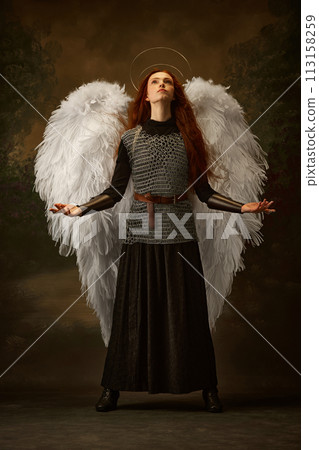 Warrior woman with golden diadem looks as angel looking up and raising hands against vintage studio background. 113158259