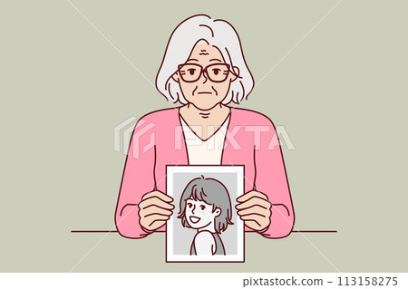 Elderly woman remembers youth, showing portrait from past, and looks at screen with slight sadness 113158275