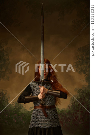 Mediaeval person, woman-knight posing looking at camera through sword against vintage background. Brave. 113158315