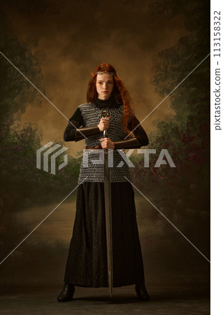 Full-length portrait of young princess in chainmail with sword posing against vintage background, showing her brave. 113158322