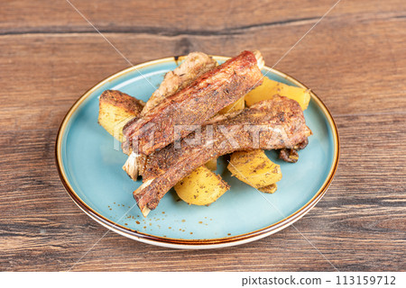 Baked pork ribs with potatoes in a plate on a wooden countertop. Baked pork ribs with potatoes in a plate on a wooden countertop. 113159712