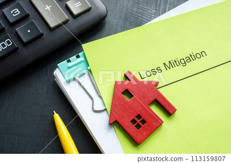 A stack of documents about loss mitigation with a figurine of a house. A stack of documents about loss mitigation with a figurine of a house. 113159807