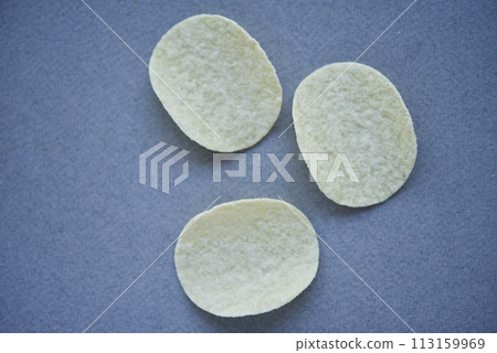 Potato chips on a gray background. Pour the chips into a saucer. A delicious snack. Potato chips on a gray background. Pour the chips into a saucer. A delicious snack. 113159969
