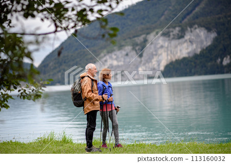 Portrait of beautiful active elderly couple hiking together in autumn mountains. Senior tourists looking at lake. 113160032