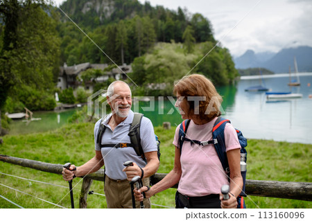 Portrait of active elderly couple hiking together in autumn mountains. Senior tourists looking at lake Portrait of active elderly couple hiking together in autumn mountains. Senior tourists looking at lake 113160096