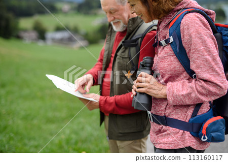 Active elderly couple hiking together in mountains, enjoying nature. Senior tourists looking at route on map. Active elderly couple hiking together in mountains, enjoying nature. Senior tourists looking at route on map. 113160117