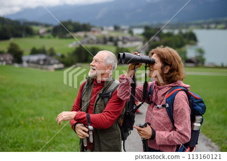 Active elderly couple hiking together in autumn mountains. Senior tourists enjoying nature look through binoculars. 113160121