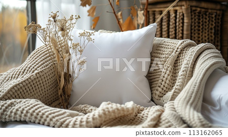 A white pillow mockup rests on a knitted blanket on a wooden couch in a cozy room 113162065