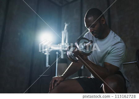 Fitness workout in gym. African American man bodybuilder picking up dumbbells in gym. Workout weight training biceps muscles with dumbbell in fitness club. Man doing sports exercise. Healthy lifestyle 113162728