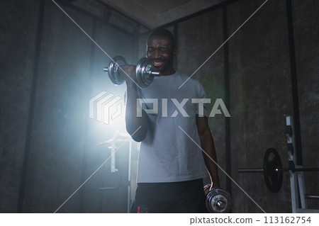 Fitness workout in gym. African American man bodybuilder picking up dumbbells in gym. Workout weight training biceps muscles with dumbbell in fitness club. Man doing sports exercise. Healthy lifestyle 113162754