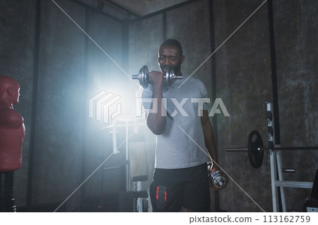 Fitness workout in gym. African American man bodybuilder picking up dumbbells in gym. Workout weight training biceps muscles with dumbbell in fitness club. Man doing sports exercise. Healthy lifestyle 113162759