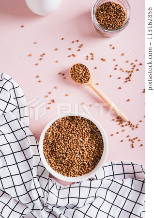 White bowl with raw whole grain buckwheat on pink background top and vertical view 113162856