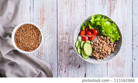 Boiled buckwheat, pieces of fresh vegetables and herbs in a bowl on the table top view web banner Boiled buckwheat, pieces of fresh vegetables and herbs in a bowl on the table top view web banner 113162866