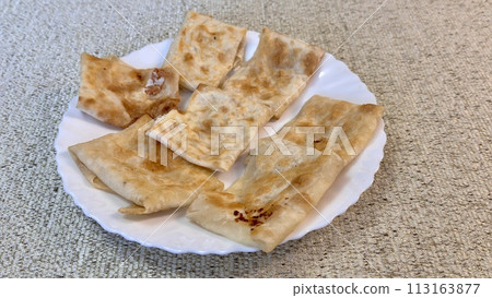 Fried pancakes-envelopes with cottage cheese, in form of envelopes in pita bread on white plate on table against background of a tablecloth 113163877