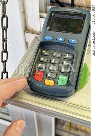 Close-up of a payment terminal lying on a table for paying for goods using plastic cards. The finger of an unknown person enters the PIN code. Close-up Close-up of a payment terminal lying on a table for paying for goods using plastic cards. The finger of an unknown person enters the PIN code. Close-up 113163924