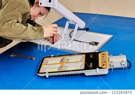 Assembling stand alone solar street light, an electrician attaches solar module and LED luminary to light arm or mounting bracket. 113163973