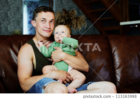 Father with baby daughter in his arms sits on leather sofa at home. 113163998