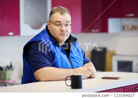 Sad large build man sits in front of kitchen island. 113164027