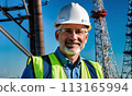 electrician engineer against background towers, gray-haired man electrician works with white helmet head, construction, energy technology industry, energy businessman, construction engineer, work 113165994