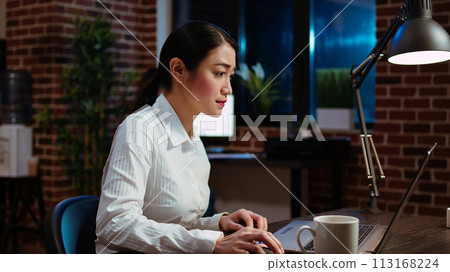 Businesswoman transcribing information from laptop to notepad, doing tasks for team project in office overnight. Worker working late at night, writing down data from computer screen 113168224
