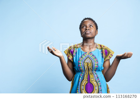 African american woman interacting with Jesus by saying grace, spiritual person with belief praying to God against blue background in studio. Religious female model saying a prayer. 113168270