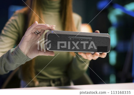 Teenage online star in home studio filming video about best bluetooth music playing devices of the year, close up shot. Focus on portable speaker reviewed by girl evaluating sound quality 113168335