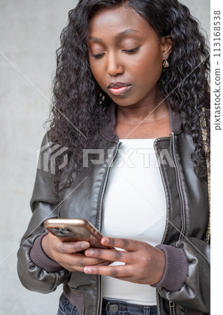 Young Woman Engrossed in Smartphone Against Gray Backdrop 113168538