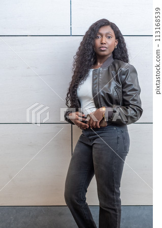 Stylish Confidence: African Woman in Urban Attire Against Modern Background 113168539