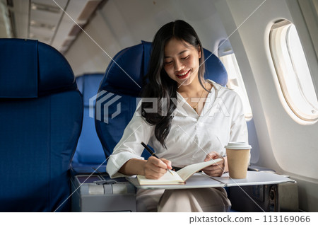 A businesswoman is taking notes in her notebook while flying to another city for a business meeting. 113169066