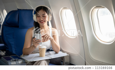 An attractive woman is using her phone and listening to music on her headphones during the flight. An attractive woman is using her phone and listening to music on her headphones during the flight. 113169108