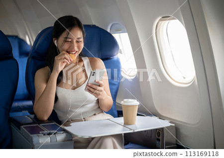 A female passenger is enjoying snacks, listening to music on her headphones during the flight. 113169118